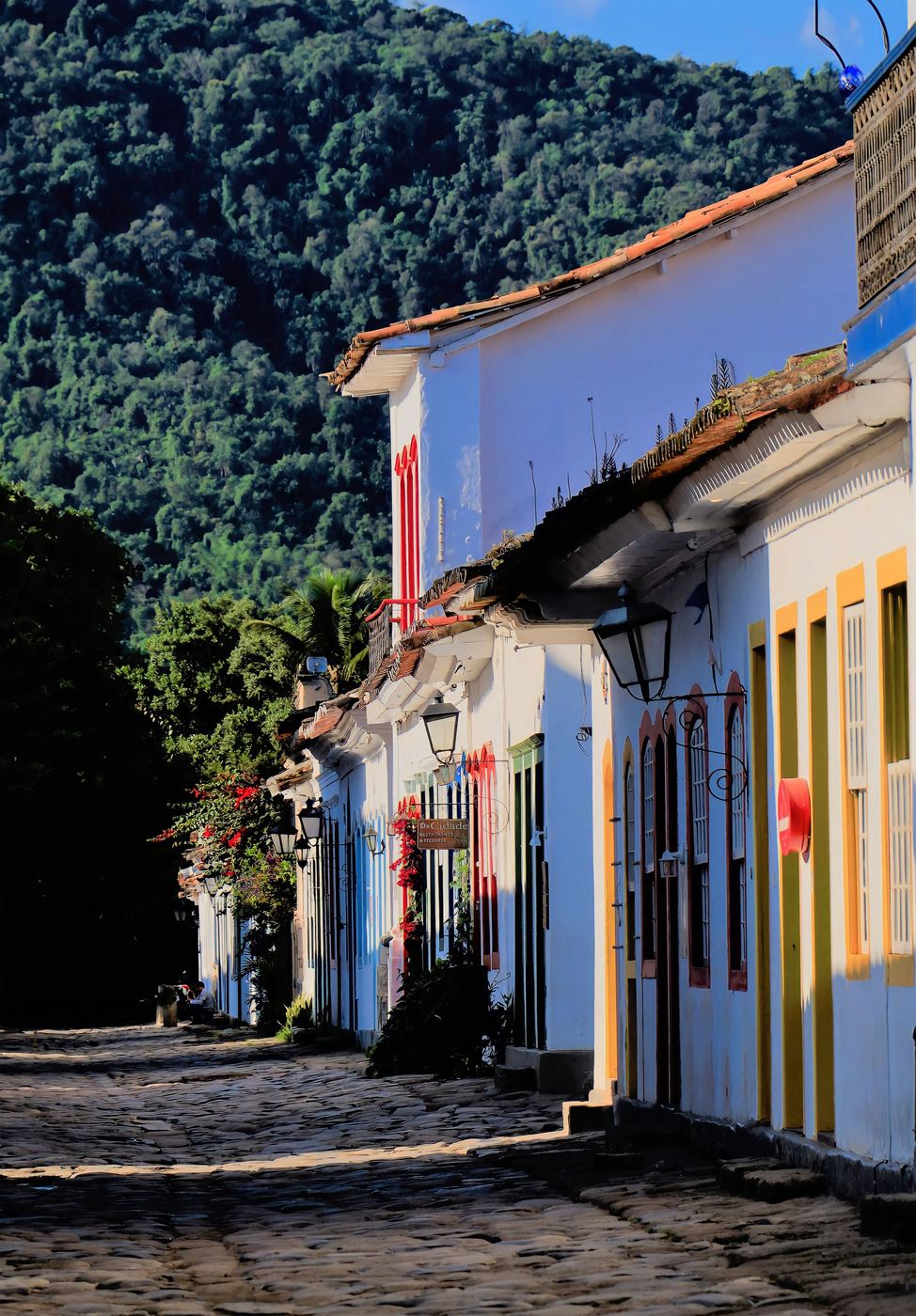 Rua de pedra do centro histórico de Paraty com casarões brancos de portas coloridas