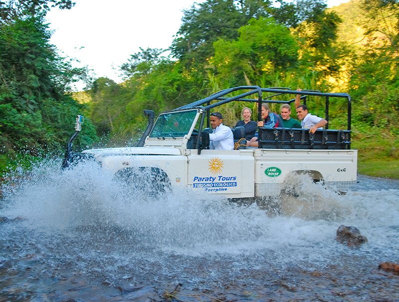 Jipe 4x4 aberto atravessando um rio, com passageiros