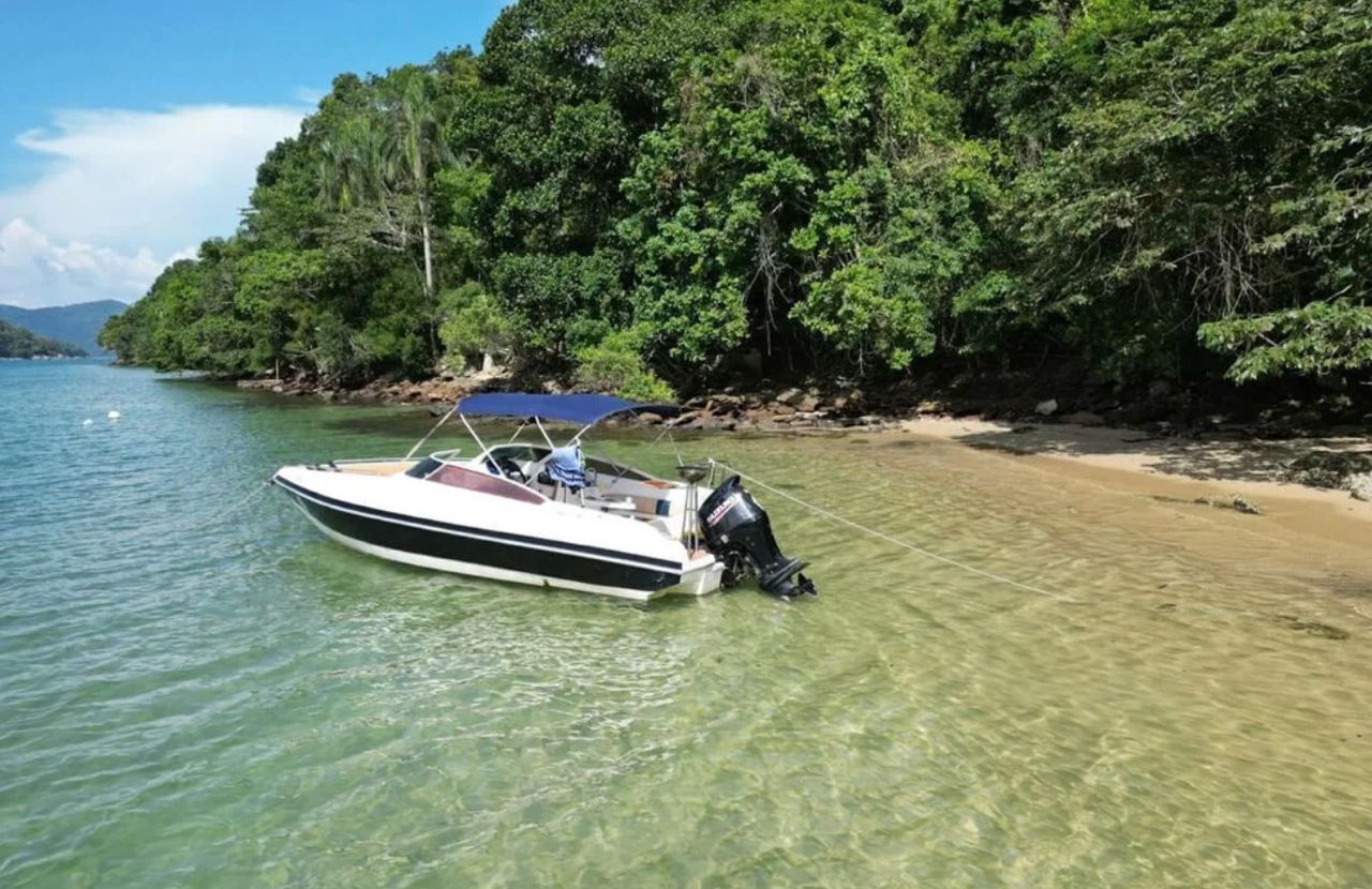Lancha ancorada na água rasa e transparente de uma praia cercada de mata